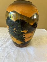 Front view of carved wooden vase showing pine trees and mountain landscape with bird in sky