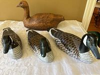 Front view of three wooden duck decoys on table showing two painted Canada goose decoys and one unpainted wooden duck decoy with broken tail.
