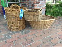 Three wicker baskets on brick floor - tall handled cylinder basket, large oval laundry basket, small rectangular weathered basket