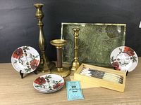 Full lot view showing 3 brass candlesticks, 4 floral patterned plates, 6 Laguiole steak utensils in box, and green marble-look tray
