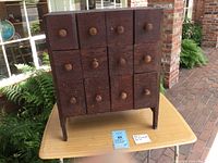 Front view of folk art 12 drawer cabinet showing 3 rows of wooden drawers with round wooden knobs and visible wear.