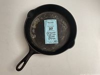 Top view of the Griswold cast iron skillet showing wear and discoloration on cooking surface with a Maxsold lot sticker in the center.