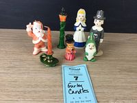 Lot of six Gurley holiday figure candles shown together on wooden surface, including Pilgrim couple, Santa, caroler, elf, and light post.