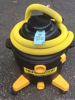 Full view of HEPA vacuum with coiled yellow hose on top showing overall condition and color.