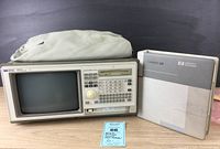 Front view of the Hewlett-Packard 1662A Logic Analyzer with screen, keypad, rotary knob, and a protective cover on top. Also showing User's Reference Manual beside it.