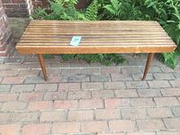 Front and side view of the wooden slatted bench showing design and wear on surface.