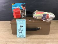 Locking cash box with attached keys, red pencil sharpener in box, staplers with staples on top of box