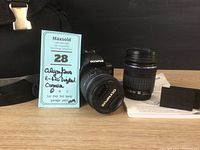 Photo showing Olympus E-620 digital camera with 14-42mm lens mounted, 40-150mm lens, two batteries, camera bag and instruction manual.