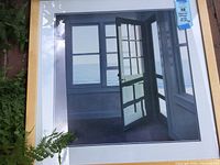 Framed ocean scape print showing a view of a door and windows looking out to the ocean, in a light wood 33 by 33 frame.