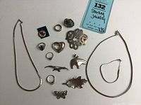 Overview photo displaying entire collection including two chain necklaces, multiple rings with stones, brooches shaped like butterfly, leaf, bird, and bear, and an oval bracelet.