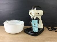 Front view of vintage Sunbeam Mixmaster mixer with two glass mixing bowls side by side on a wooden surface with black background.
