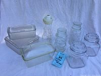All vintage glass storage containers and juice bottle displayed with lids and stopper.