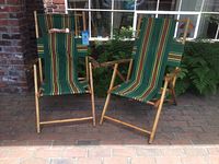 Two vintage mid century beach chairs with wooden frames and striped fabric seating and back, shown standing side by side on brick patio.