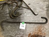Large and smaller antique farm hooks on wooden surface showing rust and wear