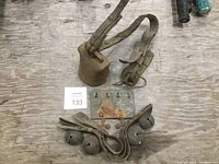 Overview of large rusted cow bell with attached leather strap, four smaller sleigh bells on leather straps, and metal weaning device