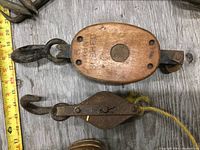 Top view of wooden pulley with metal hooks and double sheave metal pulley on wood surface with measuring tape