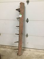 Full view of antique seeder showing wooden plank with six metal spikes extending outward.