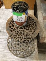 Top view of round decorative cast iron vent covers with intricate lattice patterns and a coffee can holding multiple small hardware pieces