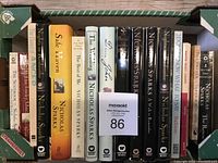 Photo showing a box with 13 Nicholas Sparks books placed upright side by side, with titles clearly legible including The Notebook, Safe Haven, The Wedding, Dear John, and others.