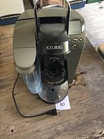 Front view of Keurig coffee maker showing water reservoir, open lid, and drip tray with star pattern perforations.