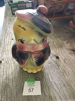 Front view of ceramic cookie jar shaped like a Scottish chick wearing a tam o'shanter hat and jacket, sitting on a wooden surface.
