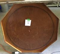Top view of the octagonal wooden crokinole board showing the circular playing surface with mostly intact pegs around the middle except one missing peg. Medium brown wood finish with visible grain.