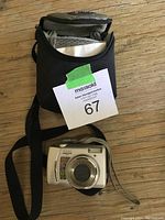 Nikon Coolpix camera front and carrying case photo on wooden floor, with MaxSold lot tag