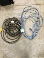 Two extension cords laid on a concrete floor, one brown and one blue with orange stripe, both coiled.