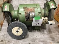 Photo of the green bench grinder showing the entire tool with two grinding wheels mounted on either side, one wire brush wheel and one abrasive wheel.