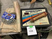 Overview photo of electric fence charger, weaning device, and fabric bags on wooden table.