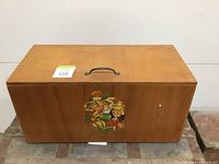 Front and top view of rectangular wooden toy box with metal handle and vintage cartoon character decals on the front.