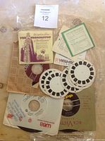 Photo showing a box for Queen Elizabeth II Coronation View-Master reels, several small vinyl records in paper sleeves, and a few View-Master reels containing image slides.