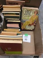 Photo showing multiple older books including Anne of Windy Poplars and Songs of the Kings arranged upright and stacked in a box