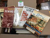 Top view of six quilting and sewing books placed on top of a cardboard box. Covers feature quilt patterns and titles related to sewing and quilting.