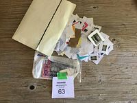 Envelope containing various loose and sleeved postage stamps scattered on wooden table, showing partial overlap and a variety of stamp backs and fronts.