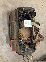 Overview of the open-top green tool bag with red trim, filled with various hand tools and a leather tool belt.