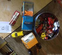Top view of small and bigger toy trucks including an orange truck, a red and silver fire truck, yellow car, and a blue truck with orange frame.