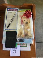 Set of unused notepads and pens stacked on a white box, including a puppy-themed notepad with attached pen and a Magnetic Attraction message notepad with pen.