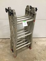 Folded ladder compacted vertically showing aluminum construction, round rungs, black knob locks on top hinge, red rubber feet at bottom.