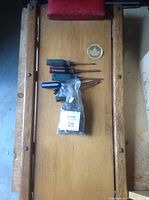 Wooden shop creeper with red padded headrest, five screwdrivers, and sealed bag of hex keys arranged on creeper surface