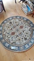 Top-down photo of round wool area rug on light wood floor showcasing floral vine pattern and blue border