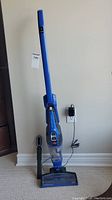 Full side view of blue Bissell Powerswift Ion Pet vacuum standing upright on charger dock, plugged into wall outlet.