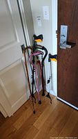 Three walking canes and two EZ Pick grabbing tools leaning against a wall near a door on wooden floor.
