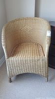 Full front view of the wicker chair on a carpeted floor next to a wall showing its shape and design.