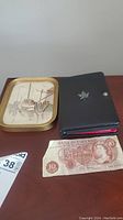Photo showing the 10 shilling note next to a black wallet and a framed artwork.