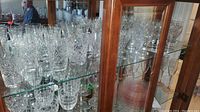 Multiple cut crystal tumblers and stemware displayed on glass shelf