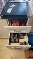 Top view of two open kitchen drawers with various cutlery and kitchen utensils, with black Keurig coffee pod holder on counter