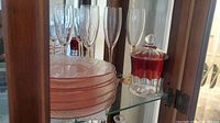 Image showing five pink stemmed champagne flutes behind six stacked pink depression glass plates and ruby cut-to-clear lidded jar on right.