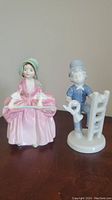 Two porcelain figurines shown side by side on a flat surface: Royal Doulton Bo Peep in pink dress and green bonnet, and Gerold Porcelain Bavaria figurine of man in blue with trumpet and ladder.