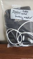 Kobo reader with charger and cord in clear Ziploc bag labeled 'Kobo works factory reset'.